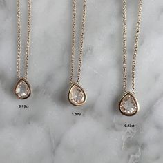 three different necklaces on a marble surface with one diamond in the middle and two diamonds at the bottom