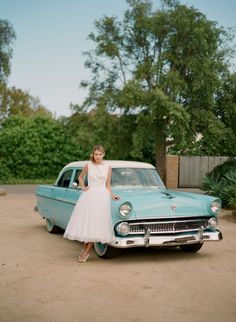 a woman in a white dress standing next to an old car