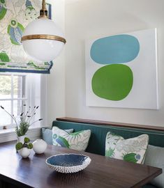 a dining room table with green and white pillows on it next to a blue couch