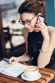 a woman sitting at a table with a cup of coffee talking on her cell phone