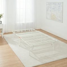 a white bed frame sitting on top of a wooden floor next to a table and chair