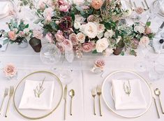 the table is set with white and gold plates, silverware, and pink flowers