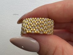 a woman's hand holding a ring with gold squares on the middle and sides