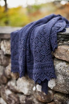 a blue knitted blanket sitting on top of a stone wall