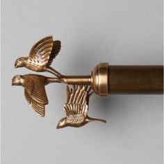 two brass birds are attached to the handle of a curtain rod that is hanging on a wall