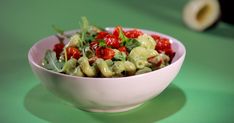 a white bowl filled with pasta covered in tomatoes and spinach sprinkles