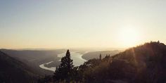 the sun shines brightly in the distance as it rises over a valley and river