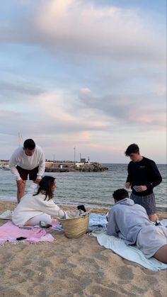 three people are sitting on the beach and one person is holding a basket with food in it