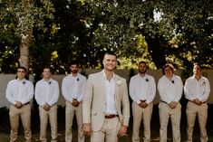 a group of men standing next to each other wearing white shirts and tan pants with ties