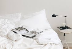 an open book on a bed with white sheets and pillows, next to a lamp