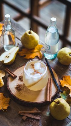 an apple cider sits on a wooden table surrounded by autumn leaves, cinnamons and apples