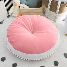 a pink round pillow sitting on top of a white floor next to a stuffed penguin