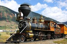 an old fashioned steam engine is on the train tracks with mountains in the back ground