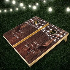 two cornhole game boards with lights on the grass and string lights in the background