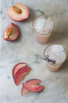 two glasses filled with ice and peaches on top of a marble table next to sliced peaches