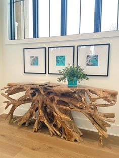 a table made out of driftwood in front of two framed pictures on the wall