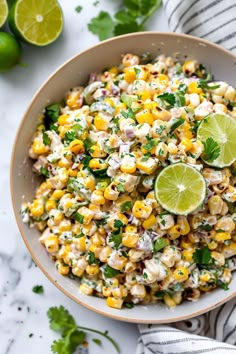 a bowl filled with corn salad next to limes