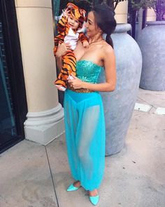 a woman in a blue dress holding a small child wearing a tiger costume on the street