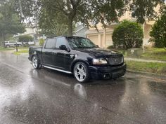 a black truck is parked on the side of the road in the rain with its hood up