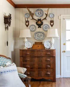 a wooden dresser topped with blue and white plates next to a deer head mounted on the wall