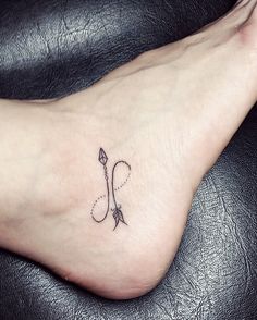 a small tattoo on the foot of a woman with an arrow and hook in it