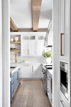 an open kitchen with white cabinets and wood flooring, along with wooden beams in the ceiling