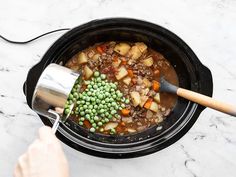 a person stirring food in a crock pot with a ladle on the side