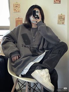 a person sitting in a chair with a cell phone up to their face and wearing a sweatshirt