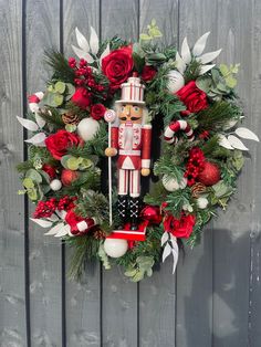 a christmas wreath with a nutcracker and red roses on the side of a wooden fence