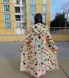 a woman is walking down the street in a crocheted coat with flowers on it