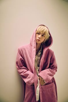 a young man in a pink robe leaning against a wall with his hands on his hips