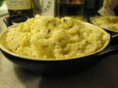 mashed potatoes in a black bowl on a counter with wine bottles and utensils