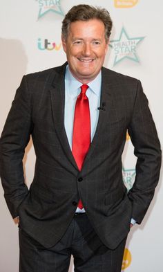 a man in a suit and red tie standing on a red carpet with his hands in his pockets