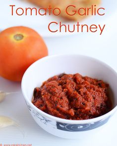 a white bowl filled with sauce next to an orange on a plate and text overlay that reads tomato garlic chutney