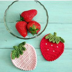 two crocheted strawberries and one strawberry in a glass bowl on a blue wooden table