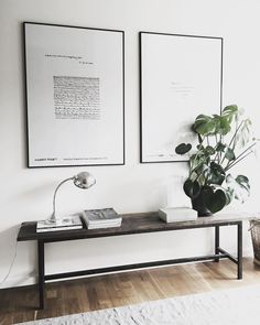 two framed pictures hang on the wall next to a table with a plant in it