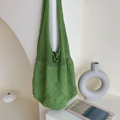 a green bag hanging on the wall next to a white vase and magazine holder with a book