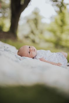 a baby laying on top of a bed next to a green tree in the background