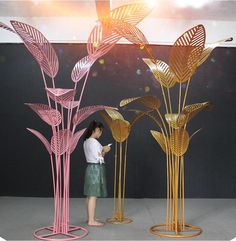 a woman standing in front of three tall metal sculptures that look like flowers and leaves