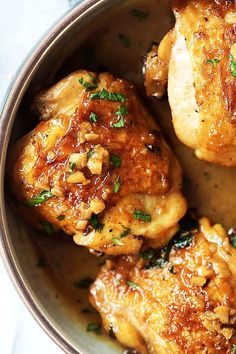 three pieces of chicken in a bowl with parsley on the top and another piece of meat below