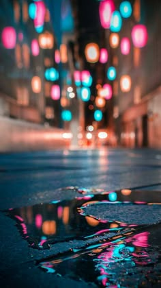 a wet street with colorful lights hanging from it's ceiling and puddles of water on the ground