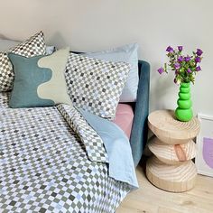 a bed with checkered sheets and pillows next to a small table with flowers on it