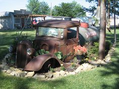 an old rusted truck sitting in the middle of a yard with plants growing out of it