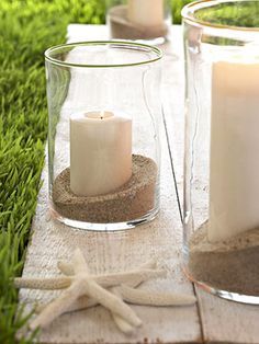 some candles are sitting in glass vases on the ground with sand and starfish