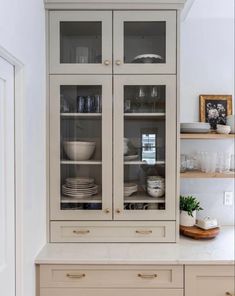 a cabinet with glass doors in the middle of a white kitchen countertop and cabinets below it