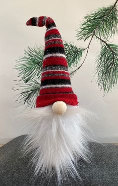 a red and black striped gnome hat on top of a rock next to a pine tree