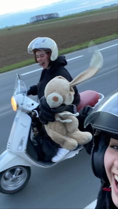 two people on a scooter with a teddy bear riding in the back seat