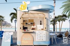 a small ice cream stand with a man working at the counter and palm trees in the background