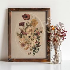 a vase filled with flowers sitting next to a painting on a white wall behind a wooden frame