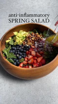 a salad with strawberries, blueberries, avocado and spinach in a wooden bowl